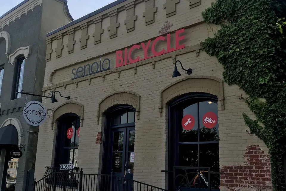 The painted brick front of Senoia Bicycle on Main Street in Senoia, with the shop's name in red letters above three arched windows and doors.
