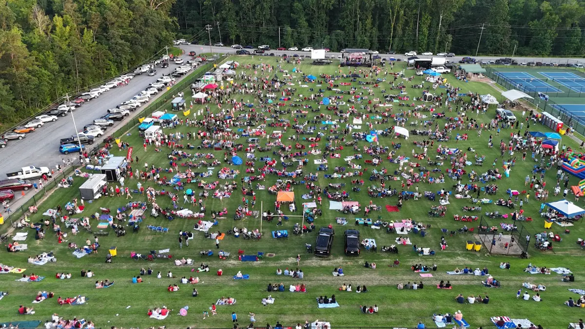 An aerial view of hundreds of families spread across a wide green field with tents and camp chairs, waiting for the Fireworks Over Newnan show to begin.